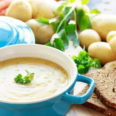 Pyszna zupa ziemniaczana przepis babci, podana w niebieskiej misce, z ziemniakami, marchewką i chlebem żytnim w tle.