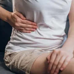 Osoba trzyma się za prawy bok, gdzie znajduje się wątroba. Czy witamina B3 może pomóc w jej dolegliwościach?