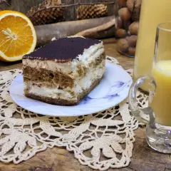 Sernik z pomarańczami i likierem pomarańczowym, obok połówka pomarańczy i kieliszek z likierem.