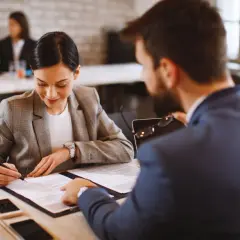 Kobieta podpisuje umowę na czas nieokreślony, siedząc przy biurku z mężczyzną.