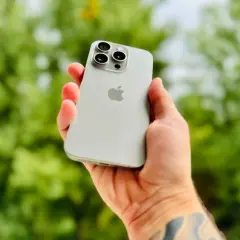 Dłoń trzyma srebrny iPhone 15 Pro Max, prezentując jego potężny aparat.