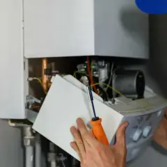 Un technicien examine l'intérieur d'une chaudière à gaz. Il tient un tournevis et une partie de l'appareil.