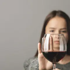 Kobieta odrzuca kieliszek czerwonego wina, symbolizując walkę z zatruciem alkoholowym.