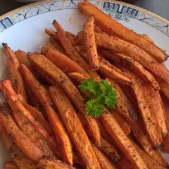 Chrupiące frytki z marchewki na talerzu, ozdobione natką pietruszki.