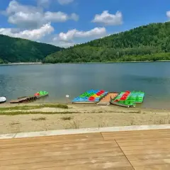 Idealne miejsce, gdzie na wakacje w Polsce: jezioro otoczone zielonymi wzgórzami, plaża i kolorowe rowery wodne czekają na gości.