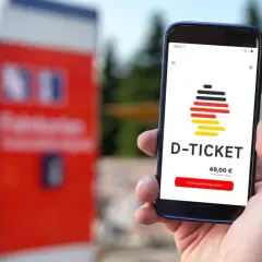 Hand hält Smartphone mit D-Ticket App. Preis 49,00 € wird angezeigt. Einfach das Deutschlandticket aktualisieren und losfahren.