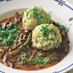 Herzhaftes Gericht mit saurer Lunge, zarten Fleischstücken in dunkler Sauce und zwei fluffigen Semmelknödeln, garniert mit frischer Petersilie.