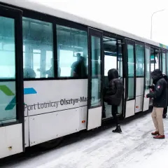 Szynobus z napisem "Port Lotniczy Olsztyn-Mazury" na tle śniegu, z pasażerami wsiadającymi.