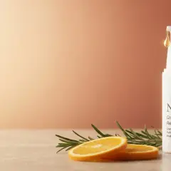 Retinol na twarz efekty: biała buteleczka serum z pompką, plasterki pomarańczy i gałązka rozmarynu.