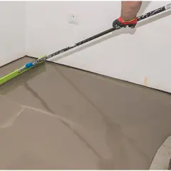 Ręka w rękawicy rozprowadza mokry tynk za pomocą narzędzia z długim trzonkiem, przypominającego **miksokret**.