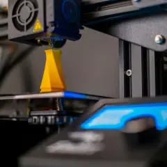 Drukarka 3D drukuje żółty obiekt, zbliżenie na dyszę i platformę roboczą.