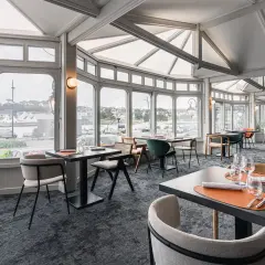 Salle de restaurant lumineuse avec vue sur le port, tables dressées et chaises modernes.