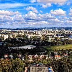 Widok na rozległe osiedla Krakowa, gdzie ceny mieszkań mogą być wysokie. W oddali widać zabudowania i zieleń.