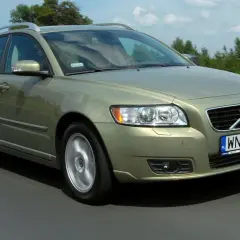 Złoty Volvo V50 1.6 diesel w ruchu drogowym, z zielenią drzew w tle.