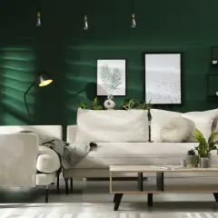 Ein gemütliches Wohnzimmer mit beiger Couch, Kaffeetisch und Pflanzen vor einer dunkelgrünen Wand. Ein Kleiderständer mit kariertem Mantel und ein trendiger Wandbehang vervollständigen das Bild.