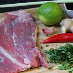 Rohes Rindersteak liegt bereit, um mit Limette, Ingwer, Chili, Knoblauch und Kräutern mariniert zu werden.