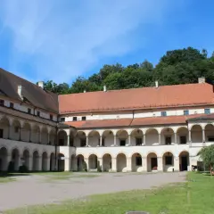 Dziedziniec zamku w Suchej Beskidzkiej z arkadowymi krużgankami i zieloną wieżą.