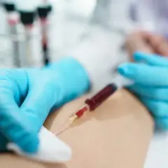 Felczer w niebieskich rękawiczkach pobiera krew do strzykawki.
