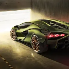Zielony Lamborghini Sian z miedzianymi felgami, wychodzący z garażu w blasku słońca.