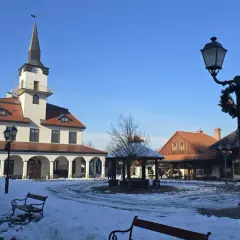 Zimowy dzień w skansenie. Miasteczko galicyjskie z ośnieżonym rynkiem, ratuszem i karczmą.