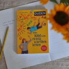 Ein Duden-Buch mit dem Titel "Jedes Kind kann richtig schreiben lernen" liegt auf einem Notizbuch. Ein Bleistift liegt daneben. Rechtschreib-training leicht gemacht.