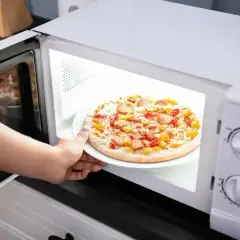 Ręka wkłada talerz z mrożoną pizzą do mikrofali. Szybki obiad gotowy!