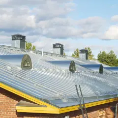 Nowoczesny dach z blachy na rabek, z kilkoma okrągłymi świetlikami i kominami.