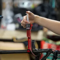 A hand uses a syringe filled with red fluid to bleed bicycle brakes. It's not as hard as you might think!