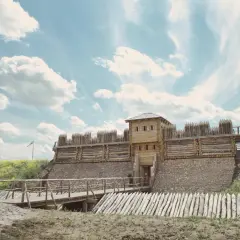Drewniany gród obronny na **środku polski**, z mostem zwodzonym i palisadą.