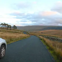 Voiture argentée sur une route sinueuse dans un paysage vallonné. La conduite à gauche est visible sur le côté de la route.