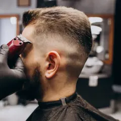 Barbero dando forma a un corte buzz cut fade con máquina. El cabello se desvanece suavemente de corto a largo.