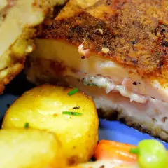 Kotlet po szwajcarsku, złocisty i chrupiący, z rozpływającym się serem i szynką w środku, podany z ziemniaczkami.