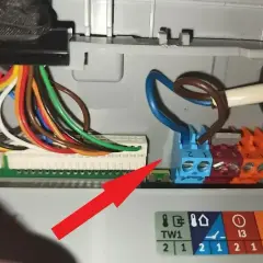 Szczegółowe podłączenie pieca gazowego kondensacyjnego. Widoczne kolorowe przewody i złącza elektryczne. Czerwona strzałka wskazuje na istotny element instalacji.