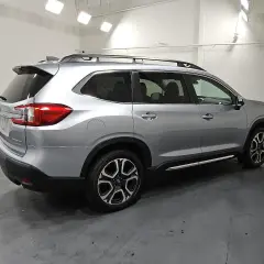 Srebrny Subaru Ascent z relingami dachowymi i przyciemnianymi szybami stoi na ciemnej podłodze.