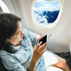 Kobieta z telefonem siedzi przy oknie w samolocie Ryanair. Widok na chmury z góry.