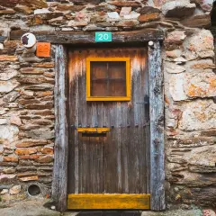Puerta de madera rústica en una pared de piedra en la serrada de la fuente. Números 20, 28 y 18 adornan la entrada.