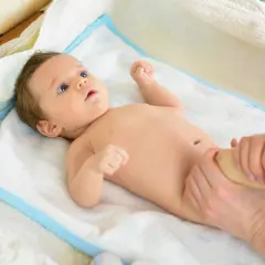 Malutki siusiak niemowlaka podczas masażu nóżek. Dziecko leży na białym ręczniku z niebieskim obszyciem.