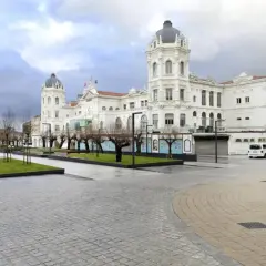Edificio blanco con cúpulas en la plaza Italia Santander. Árboles desnudos y césped verde.