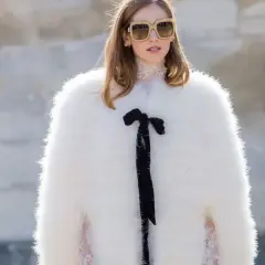 Estilo maximalismo: mujer con abrigo blanco de pelo, gafas grandes y lazo negro.