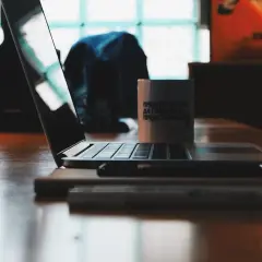 Laptop na drewnianym stole, obok kubek. Zastanawiasz się, jak wygasić ekran w laptopie?