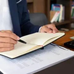 Mężczyzna w garniturze notuje w dzienniku, analizując dokumenty. Szybki odpis księgi wieczystej online ułatwia pracę.