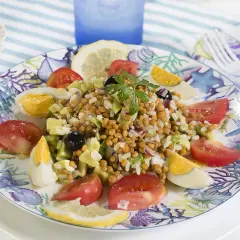 Deliciosa ensalada de lentejas y arroz con huevo duro, tomate, aguacate y aceitunas, servida en un plato con motivos marinos.