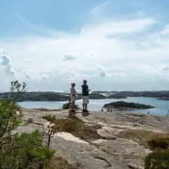 Två personer njuter av utsikten från Vetteberget i Fjällbacka. Vackert väder med moln och sol över skärgården.