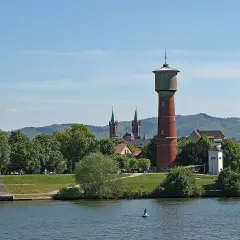 Wasserturm und Kirchtürme über grünen Bäumen, die die ladenburg altstadt säumen, mit Fluss im Vordergrund.