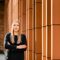 Kobieta w czarnym garniturze stoi ze skrzyżowanymi rękami na tle nowoczesnej fasady.