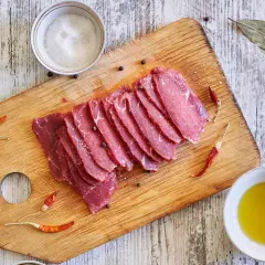 Filete de ternera crudo, cortado en finas lonchas, sobre tabla de madera con sal, pimienta, guindillas y aceite de oliva.