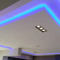 Nowoczesny sufit podwieszany z niebieskim podświetleniem LED. Widać rozmieszczenie punktów świetlnych i taśm LED, tworzących efektowną ramę.