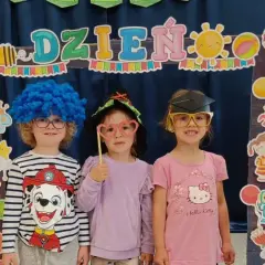 Dzieci w przedszkolu w strojach i z rekwizytami pozują do zdjęcia na tle dekoracji z napisem "Dzień Dziecka".