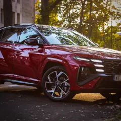 Czerwony Hyundai Tucson 4 w sportowej wersji N Line zaparkowany na tle jesiennych drzew i kamienicy.