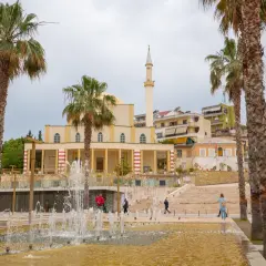 Fontanna i palmy przed meczetem w Durrës, Albania. Ludzie spacerują po placu.